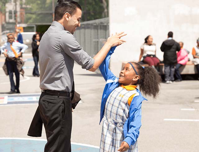 NYC Public Schools - Teacher and elementary school scholar high fiving in the school yard