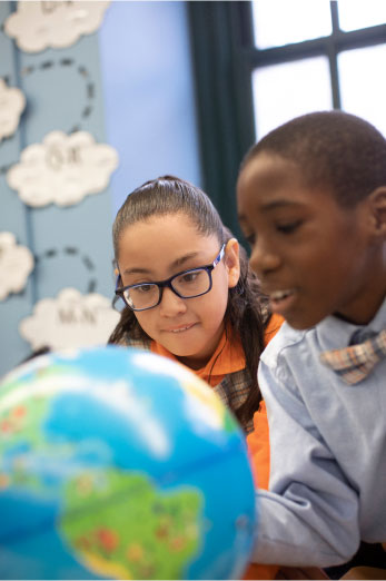 NYC Charter Schools - Two middle school scholars huddled over a classroom globe.