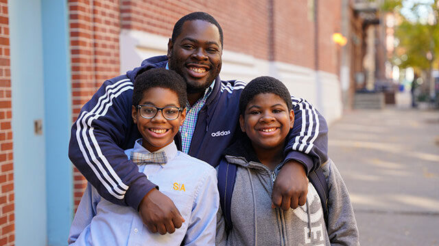 Outdoor photo of SA parent with 2 scholars smiling.