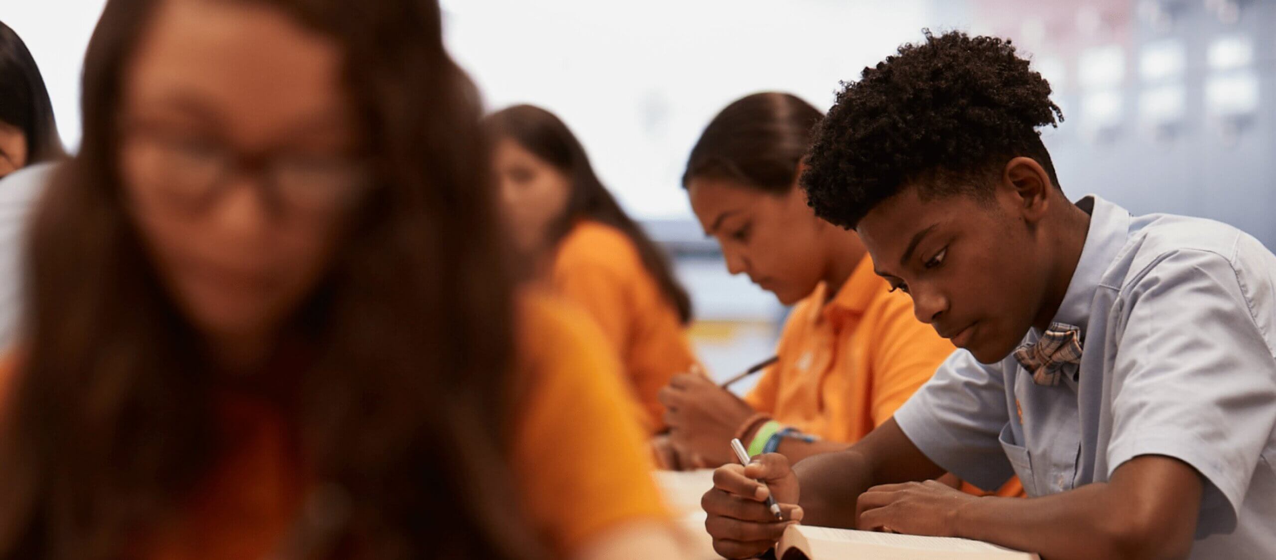 Students writing in notebooks in a classroom setting.