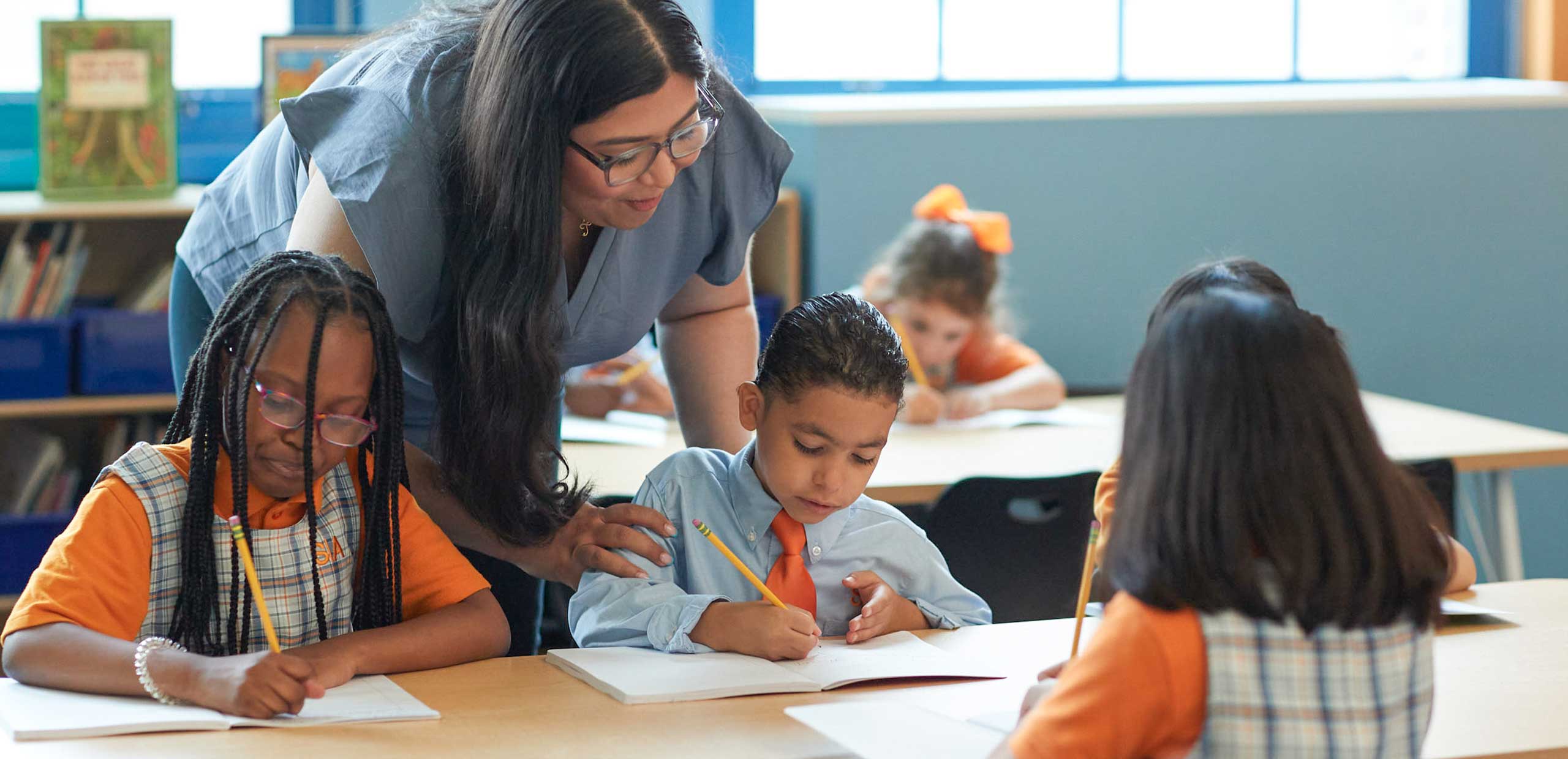 students working in a notebook with teacher helping