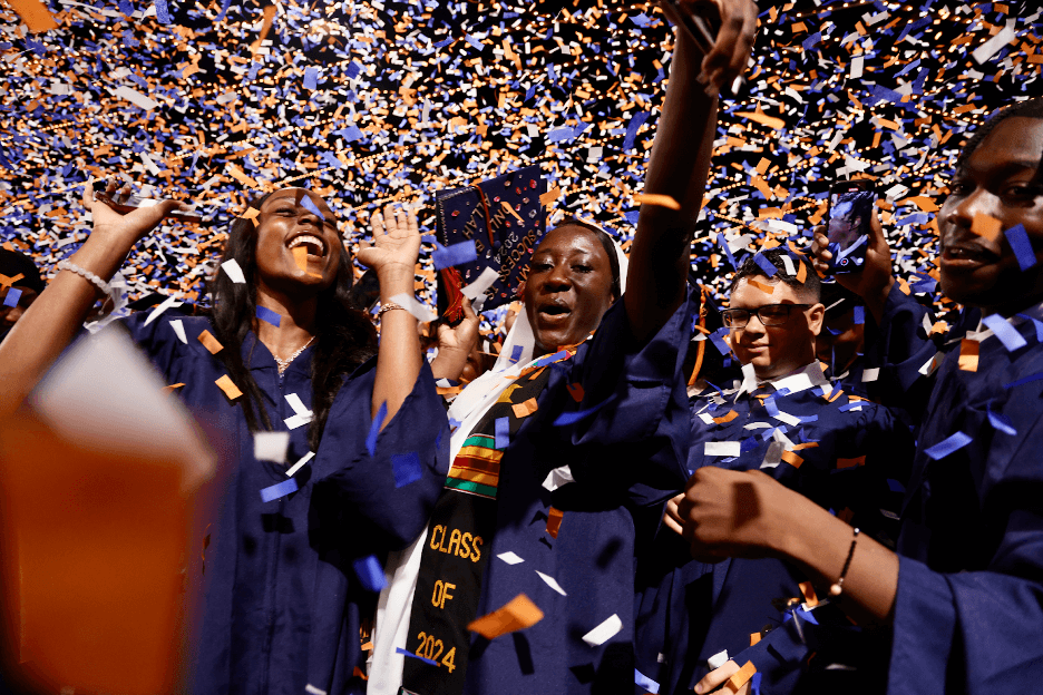 Graduates celebrating with confetti, wearing gowns and smiling joyfully.
