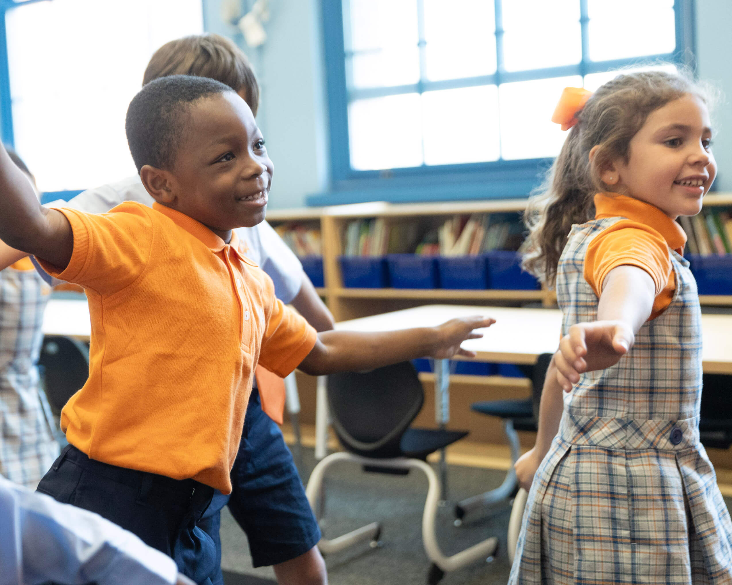A group of students standing up with their hands out engaging in a classroom activity.