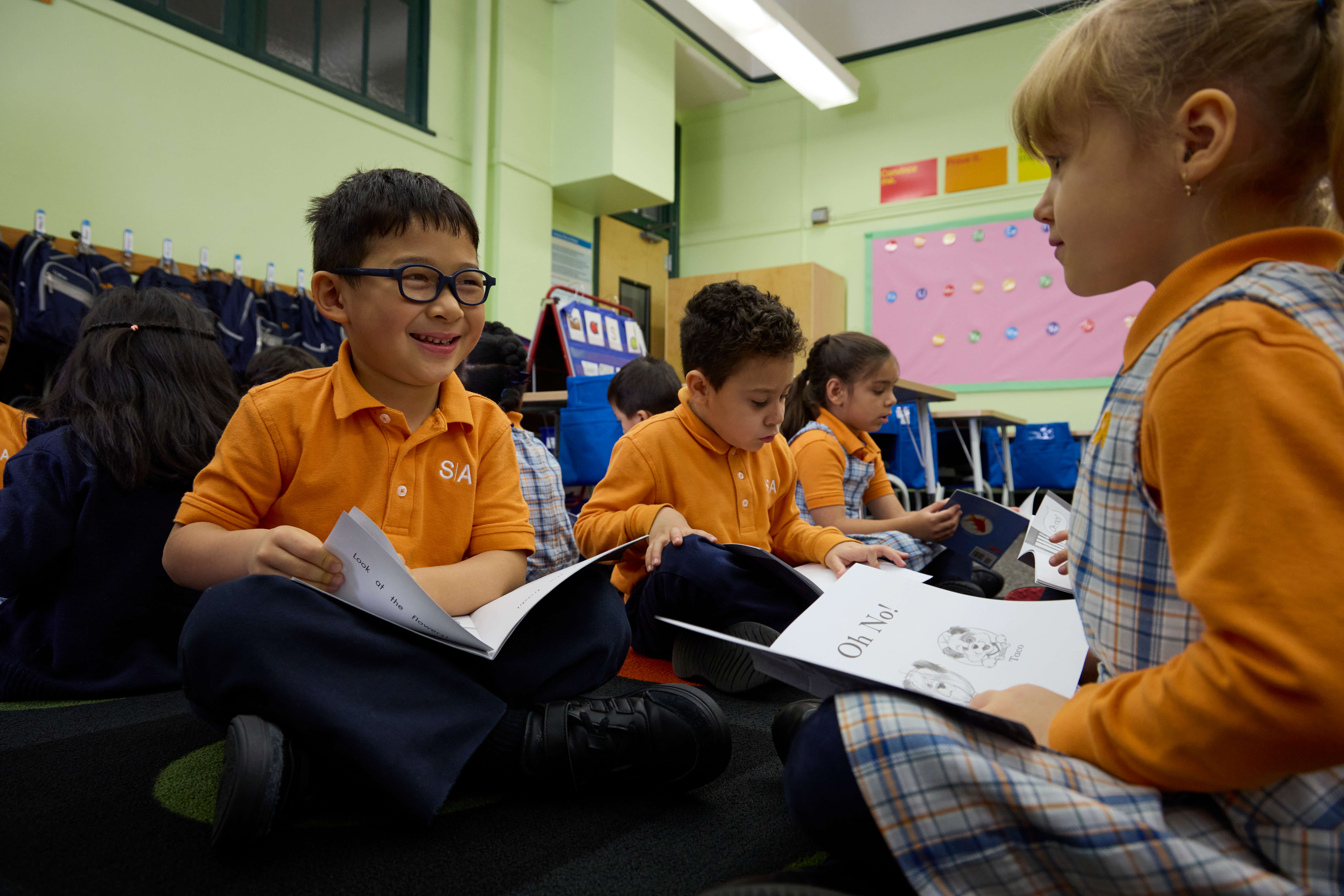 A group of children sitting cross-legged on the floor reading in a classroom.